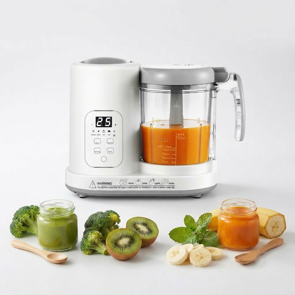 A white and gray baby food maker with a clear container filled with orange puree, shown on a light gray background with baby food jars, broccoli, kiwi, and banana slices arranged in front.