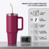 A dark magenta insulated travel tumbler with a handle, clear lid, and beige straw, shown beside a fulfillment process diagram and a small inspection label on a light gray background.