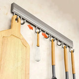 Kitchen utensil holder with hooks holding a wooden cutting board and various utensils on a light-colored wall.