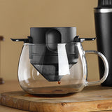 Clear glass teapot with black lid and handle on a wooden surface