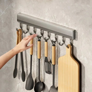 Wall-mounted kitchen utensil holder with various tools and a cutting board on a gray wall.