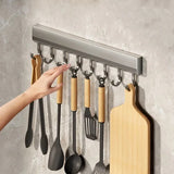 Wall-mounted kitchen utensil holder with various tools and a cutting board on a gray wall.